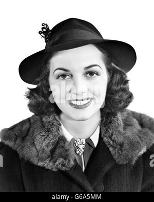 1940s sorridente BRUNETTE ritratto di donna indossa HAT COAT collare di pelliccia guardando la fotocamera Foto Stock