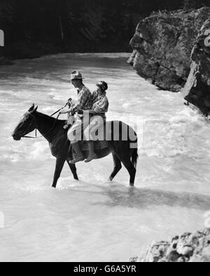 1930s GIOVANE DONNA UOMO A CAVALLO TRA STREAM donna di braccia intorno all uomo di vita Foto Stock