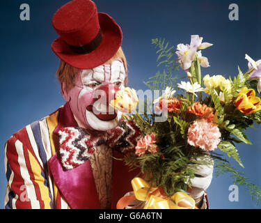 Anni Settanta ritratto HAPPY CIRCUS CLOWN INDOSSANDO TINY RED TOP HAT STRIPED COSTUME BIG bow tie odore di bouquet di fiori Foto Stock