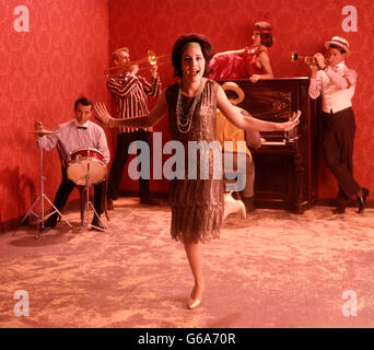 1920s SPEAKEASY SCENA DONNA ENCA ARGENTO ABITO BORDATO FACENDO IL CHARLESTON NELLA PARTE ANTERIORE DI UNA BANDA Foto Stock