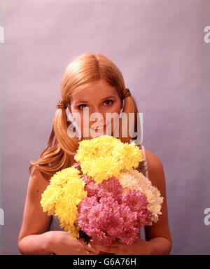 Anni Settanta giovane donna attraente ragazza bionda bionda HOLDING bouquet di fiori rosa gialla pigtail guardando la fotocamera Foto Stock