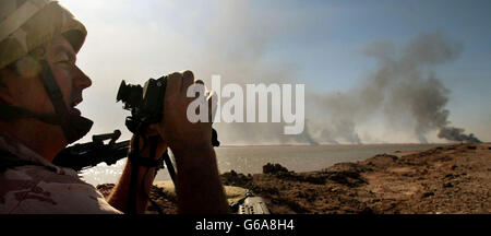 Un soldato in servizio di ingresso dal 29 Commando Regiment Royal Artillery osserva l'attività in prima linea a sud-est di Basra nel sud dell'Iraq, mentre gli incendi provenienti dai contatti nemici bruciano lungo la strada verso la città. La Gran Bretagna ha detto che, sebbene le forze statunitensi-britanniche si chiudessero a Baghdad, la caduta del leader iracheno Saddam Hussein potrebbe richiedere molto più tempo. Foto Stock