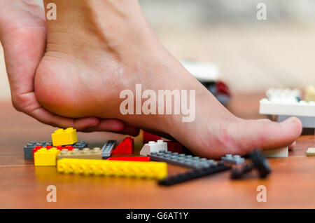 A piedi si fa male con alcuni legos sul pavimento. Vari colori, rosso, bianco, giallo, grigio, nero Foto Stock