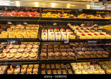 Una selezione di invitanti torte sul display in un armadio di vetro. Questi sono fatti di fresco e una vasta gamma di dolci e delizie sono offerti. Foto Stock