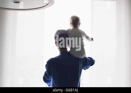 Padre figlio che porta sulla spalla, guardando fuori della finestra insieme Foto Stock