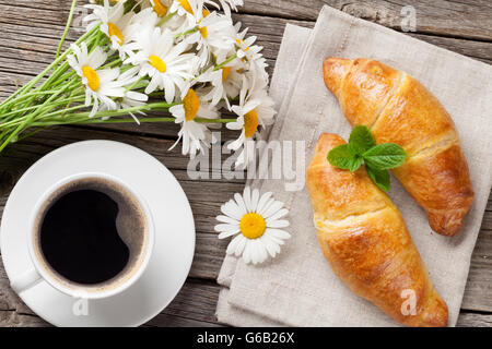 Croissant, tazza di caffè e camomilla bouquet di fiori su un tavolo di legno. Vista dall'alto. Concetto di colazione Foto Stock