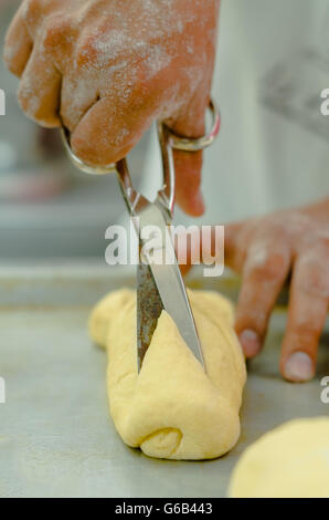 Fornai mani tenendo le forbici sopra preparato di pasta di pane rotolo Foto Stock