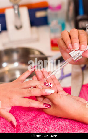 Closeup femmine mani getting manicure trattamento da donna applicazione liquido trasparente nel salone di ambiente, rosa superficie di asciugamani, sfondo sfocato prodotti Foto Stock