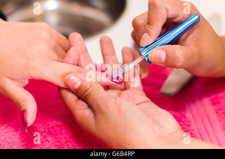 Closeup femmine mani getting manicure trattamento da donna utilizzando la spazzola piccola in salone ambiente, rosa superficie di asciugamani, sfondo sfocato prodotti Foto Stock