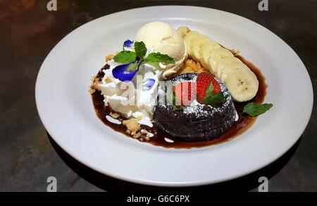 Il cioccolato fondente torta lavica decorata con spolverata di zucchero a velo, fragole fresche, banana e gelato Foto Stock