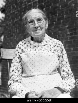 1930s ritratto donna anziana indossando occhiali abito stampa Bavaglino bianco grembiule Foto Stock