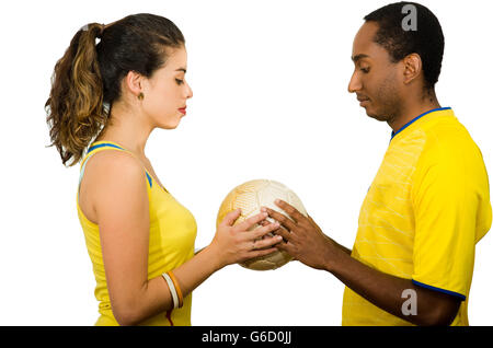 Affascinante coppia interraziale giallo da indossare magliette da calcio tenendo palla tra ogni altro, profilo angolare bianco di sfondo per studio Foto Stock