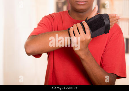 Uomo in camicia rossa vestita di nero polsiera supporto sulla mano destra e il braccio di presa con altri Foto Stock