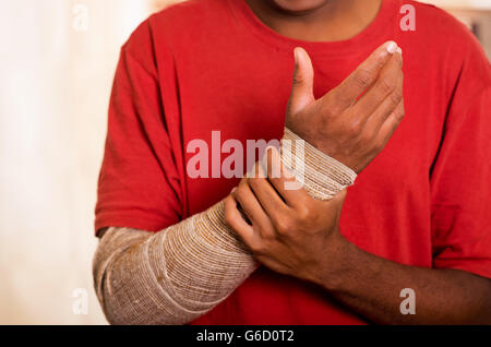 Closeup Uomo in camicia rossa indossando grande bendaggio grigio sulla parte inferiore destra del braccio di supporto, con l'altra mano Foto Stock