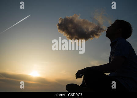Silhouette di uomo di fumare un tubo nel cappuccio al tramonto. Fotografo in un cappello da baseball di fumare un tubo al tramonto sul mare.Travel, avventura, meditazione e rilassamento, vacanza. Foto Stock