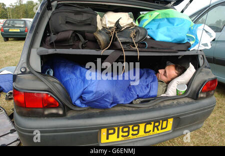 Un festaiolo dorme nel bagagliaio di un'auto al festival musicale V2003 a Hylands Park, Chelmsford, Essex. Migliaia di festaioli continuavano a godersi il sole il secondo giorno del festival con band come Inspiral Carpets, Morcheeba e David Grey, con i Red Hot Chili Peppers che portavano a termine l'evento. Foto Stock