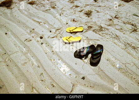 Una coppia di uomo e donna " flip flop sandali su sabbia modellato da Ocean Tides. Foto Stock