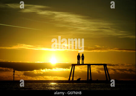 Il sole sorge sopra la scultura 'COPPIA' di Sean Henry sulla pausa acqua a Newbiggin-by-the-Sea, Northumberland. Foto Stock