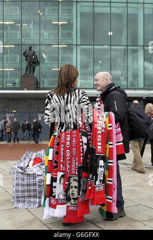 Un venditore di sciarpe al lavoro fuori di Old Trafford prima della partita, la statua di Sir Matt Busby può essere visto sullo sfondo Foto Stock