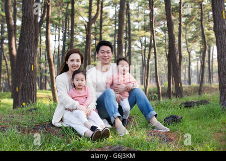 Felice famiglia asiatica seduta su erba, in posa nella foresta Foto Stock