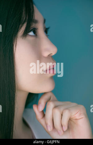 Donna che guarda lontano nel pensiero con la mano sotto il mento Foto Stock