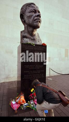 Un uomo depone fiori dalla statua di Nelson Mandela, ex presidente del Sud Africa, al lato del Royal Festival Hall sulla riva sud di Londra, dopo la notizia che era morto ieri sera dopo una lunga malattia. Foto Stock