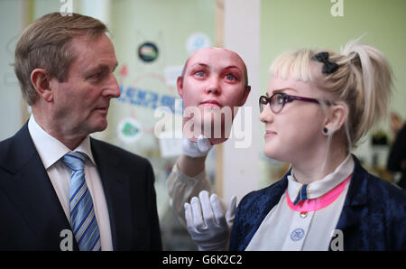 Taoiseach Enda Kenny pone con lo studente Ling Heaney e una maschera come egli aiuta a lanciare il programma di quattro nuove mostre per il 2014 presso la Science Gallery al Trinity College. La maschera è stata creata usando tracce di DNA umano trovato su mozziconi di sigaretta che litterano le strade di Dublino che sono stati portati in un laboratorio ed è stata eseguita un'estrazione di DNA. Certe regioni del DNA sono state amplificate usando una tecnica chiamata reazione a catena PCR-polimerasi. Ciò rende possibile studiare certe regioni del genoma che tendono a variare da persona a persona, note come polimorfismi di nucleotide singolo (SNP). Foto Stock