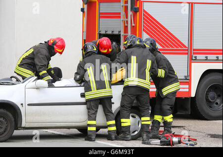 Coraggiosi vigili del fuoco alleviare un infortunato dopo incidente di automobile Foto Stock