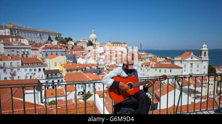 Busker suonando la chitarra nel sole caldo di Lisbona con i tetti rossi di Alfama, la città vecchia, in background. Foto Stock