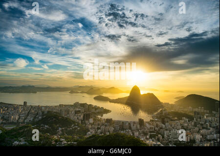 Scenic sunrise a Rio de Janeiro in Brasile si illumina golden sulla baia di Guanabara con uno skyline silhouette di Sugarloaf Mountain Foto Stock