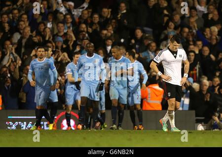 John Arne Riise di Fulham appare sconsolato dopo che Jesus Navas (oscurato) della città di Manchester ha segnato il terzo gol della sua squadra e celebra con i compagni di squadra Foto Stock