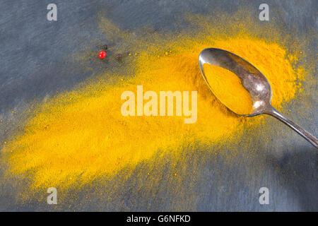 Giallo curry in polvere in cucchiaio d'argento, isolato su sfondo di ardesia. Foto Stock