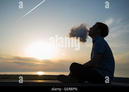 Silhouette di uomo di fumare un tubo nel cappuccio al tramonto. Fotografo in un cappello da baseball di fumare un tubo al tramonto sul mare.Travel, avventura, meditazione e rilassamento, vacanza. Foto Stock