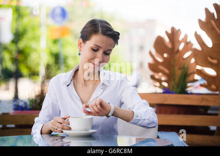 Moderno e giovane donna seduta in un bar e in attesa che qualcuno guardando a lei orologi Foto Stock