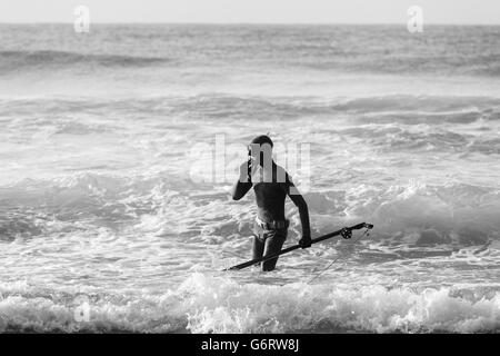 Non identificato subacqueo con la pesca subacquea pistola sulla spiaggia entra nell oceano onde Foto Stock