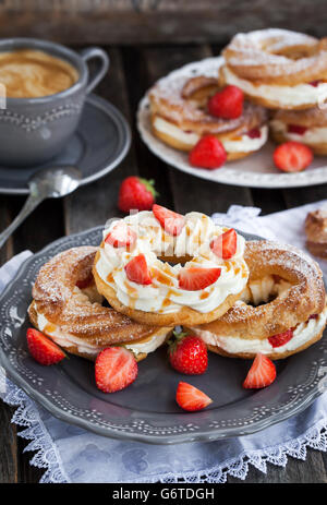 Soffio di crema anelli (bignè) decorate con fragole fresche e salsa di caramello Foto Stock