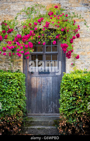 Rose rosse sulla porta di casa cottage in Cotswolds, Gloucestershire, England, Regno Unito Foto Stock
