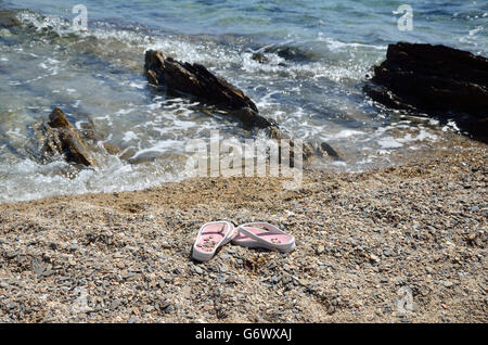 Bianco-rosa flip-flop a sinistra sulla spiaggia di sabbia con il mare poco profondo in background Foto Stock