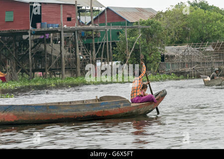 Madre con bambino la polarizzazione di una piroga accanto a palafitte, Kampong Phlluck, Tahas fiume Tonle Sap, Cambogia Foto Stock