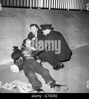 Un poliziotto in uniforme si piega e assiste un uomo che sembra essere stato ferito nelle lotte di dimostrazione al di fuori dell'ambasciata degli Stati Uniti a Grosvenor Square, Londra. I manifestanti, la maggior parte dei quali negli ultimi anni dell'adolescenza o all'inizio degli anni '20, e con almeno 2000 anni, protestavano contro il blackade americano di Cuba, annunciato in un discorso del presidente Kennedy di Washington. Foto Stock