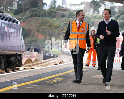 Il primo ministro David Cameron (a destra) cammina con il direttore della stazione Ian Mundy durante una visita alla stazione ferroviaria di Dawlish, Devon, dopo la riapertura della linea ferroviaria distrutta dalla tempesta. Foto Stock