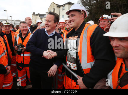 Il primo ministro David Cameron stringe le mani con l'operatrice ferroviaria Ross McCulloch, la cui t-shirt mostra le immagini della linea ferroviaria danneggiata alla stazione ferroviaria di Dawlish durante una visita a Dawlish, Devon, dopo la riapertura della linea ferroviaria distrutta dalla tempesta. Foto Stock