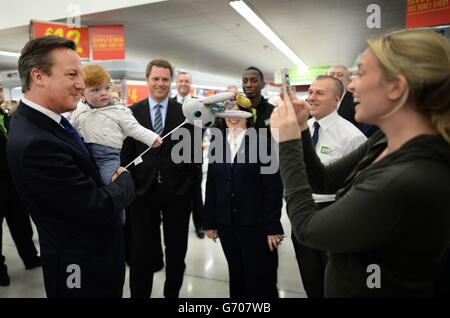 Il primo ministro David Cameron incontra il personale e gli acquirenti, tra cui Tara Leniston e il suo figlio di 11 mesi Luca ad Asda a Clapham, a sud di Londra, dove ha discusso i 12,000 nuovi posti di lavoro che la catena di supermercati creerà nei prossimi cinque anni. Foto Stock