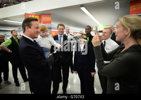 Il primo ministro David Cameron incontra il personale e gli acquirenti, tra cui Tara Leniston e il suo figlio di 11 mesi Luca ad Asda a Clapham, a sud di Londra, dove ha discusso i 12,000 nuovi posti di lavoro che la catena di supermercati creerà nei prossimi cinque anni. Foto Stock