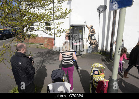 La gente si affollano intorno ad un nuovo pezzo di arte di strada dei graffiti, sospettato di essere un Banksy, che apparve sul lato di una casa su Fairview Road adiacente a St. Anne's Terrace, Cheltenham. L'opera, che mostra tre figure che ascoltano una conversazione in una scatola telefonica, si trova a poche miglia di distanza dalla sede centrale della comunicazione del governo (GCHQ), che è responsabile di fornire informazioni e informazioni di segnalazione al governo britannico e alle forze armate. Foto Stock