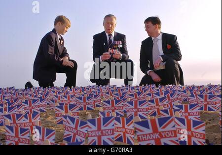 Fred Matthews (centro), veterano della seconda Guerra Mondiale, di Poole in Dorset, legge un messaggio scritto da un membro della Legione Britannica reale su una bandiera di Union Jack posta sulle sabbie di Sword Beach a Hermanville, in Normandia, nel nord della Francia, mentre si unisce al figlio Chris (a destra) e al nipote Lee Edwards, 12. Fred, che ha servito nella Marina reale su HMS Jude durante la seconda Guerra Mondiale, stava scherzando molti altri veterani che stavano ritornando in Normandia per il 60° anniversario di oggi del D-Day. La Legione Britannica reale ha piantato più di 1,520 unioni Jacks nella sabbia per pentire il numero di soldati britannici che hanno perso la vita il D-Day Foto Stock