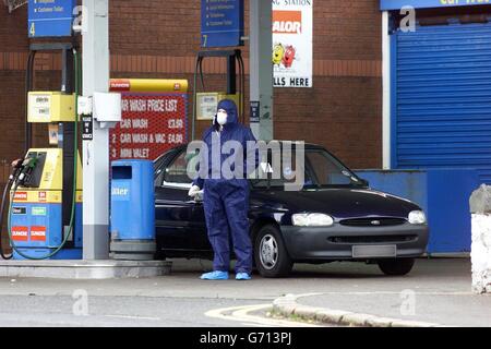 Un ufficiale di polizia si trova, presso una stazione di rifornimento di benzina sulla Antrim Road, a Belfast, accanto a una macchina in cui il corpo di una donna asiatica è stato trovato nel stivale all'inizio della giornata. Sono stati arrestati due uomini, anche ritenuti asiatici. Foto Stock