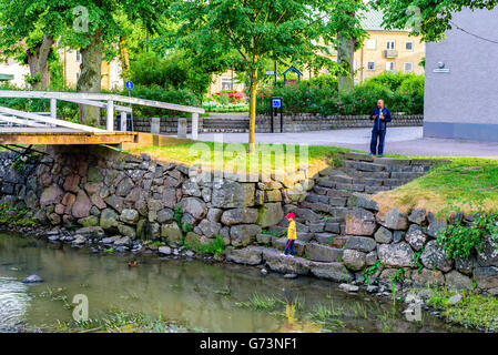 Soderkoping, Svezia - 19 Giugno 2016: Boy bambino in piedi sulla scalinata di pietra guardando il germano reale nel fiume Storan. Maschio adulto per Foto Stock