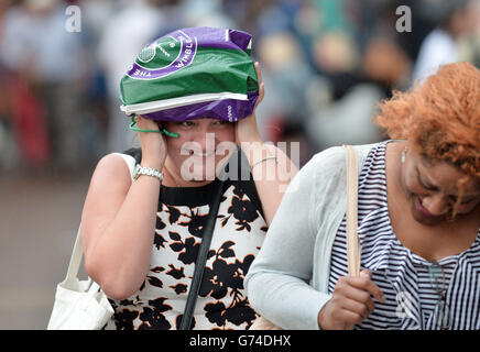 Un tifoso di tennis si ripara dalla pioggia sotto una borsa di trasporto durante il giorno uno dei Campionati di Wimbledon all'All England Lawn Tennis and Croquet Club, Wimbledon. Foto Stock