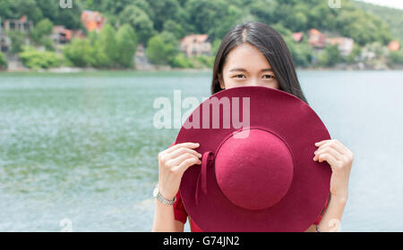 Moda Donna holding hat in piedi di fronte ad un lago Foto Stock